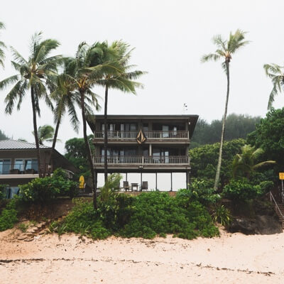 three storey home sitting on the beach surrounded by palm trees